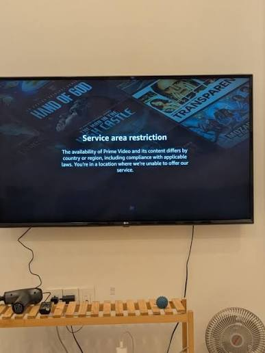 A wall-mounted TV displaying an Amazon Prime Video "Service area restriction" error message stating content is unavailable in the current location.